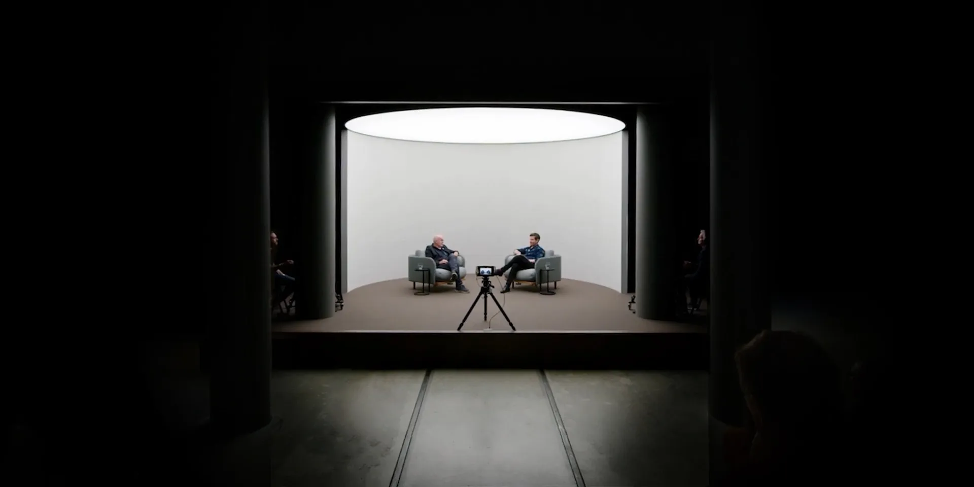 A lit stage within a in darkened exhibition space behind the 100 Climate Conversations logo.