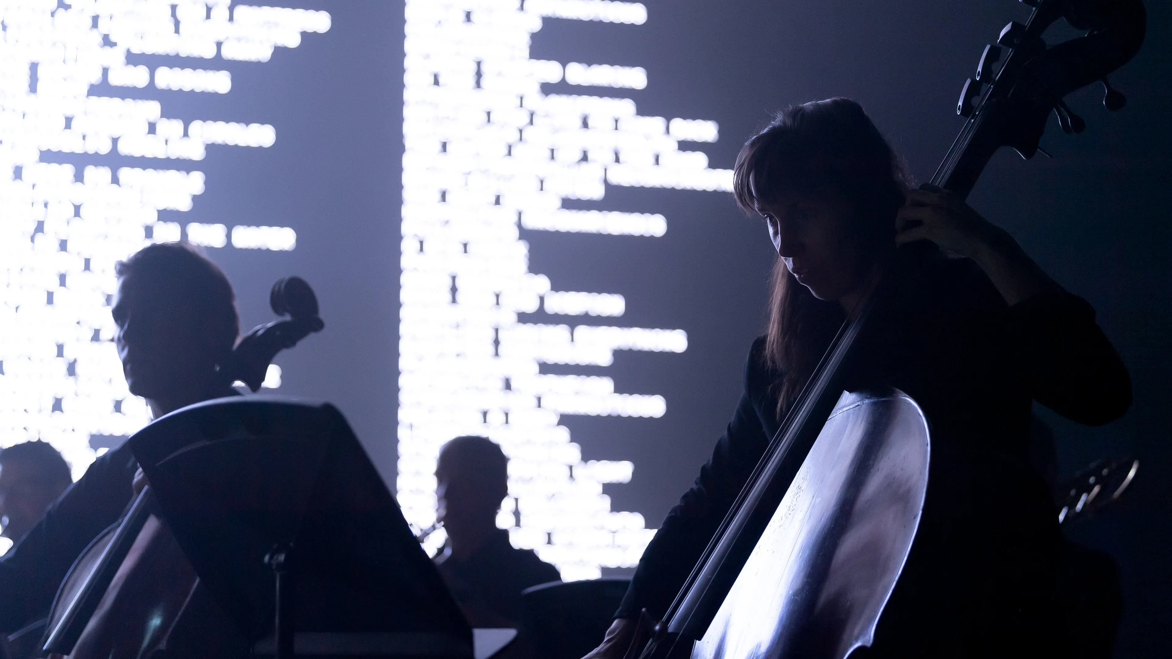 Woman playing double bass in front of large LED screen.