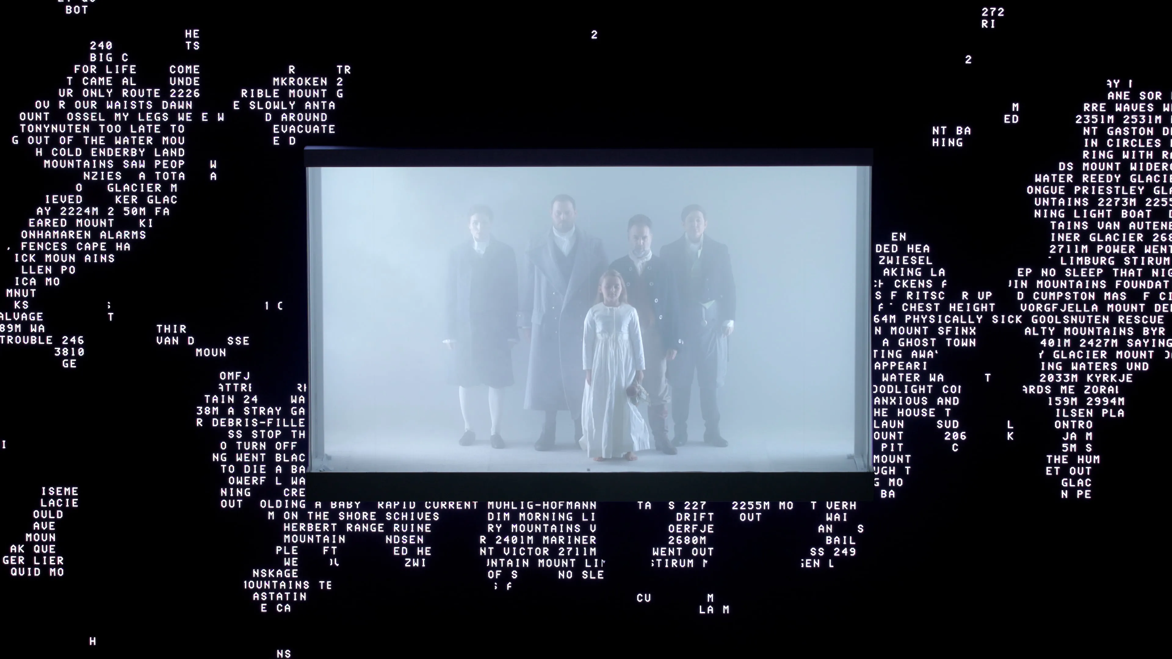 Performers standing inside a fog-filled box, surrounded by a large LED screen depicting fragmented white text on black.