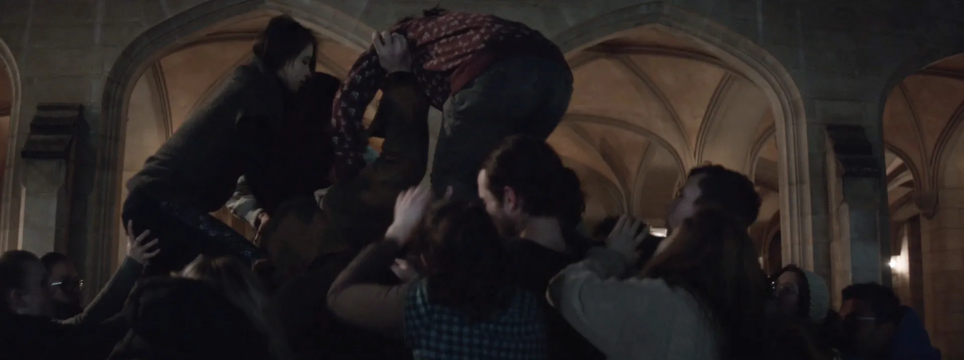 A group of people climbing on top of one another in front of old sandstone architecture at night.