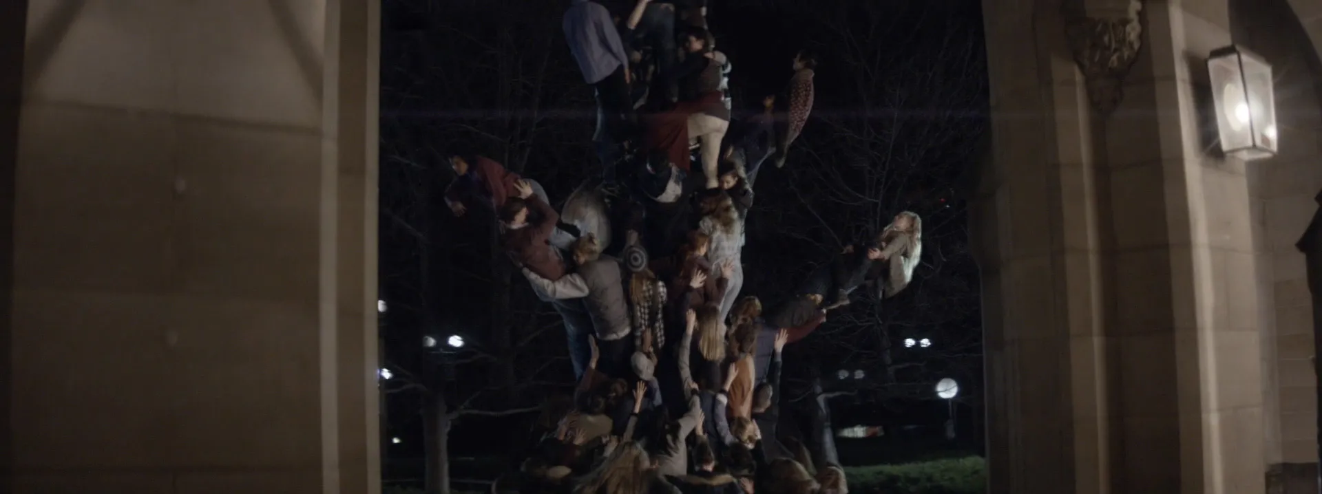 Dozens of people standing on top of one another, forming the shape of a tree.