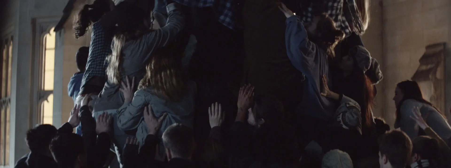 Dozens of people standing on top of one another, supporting each other with their hands raised. Together they form a wide trunk-like structure.