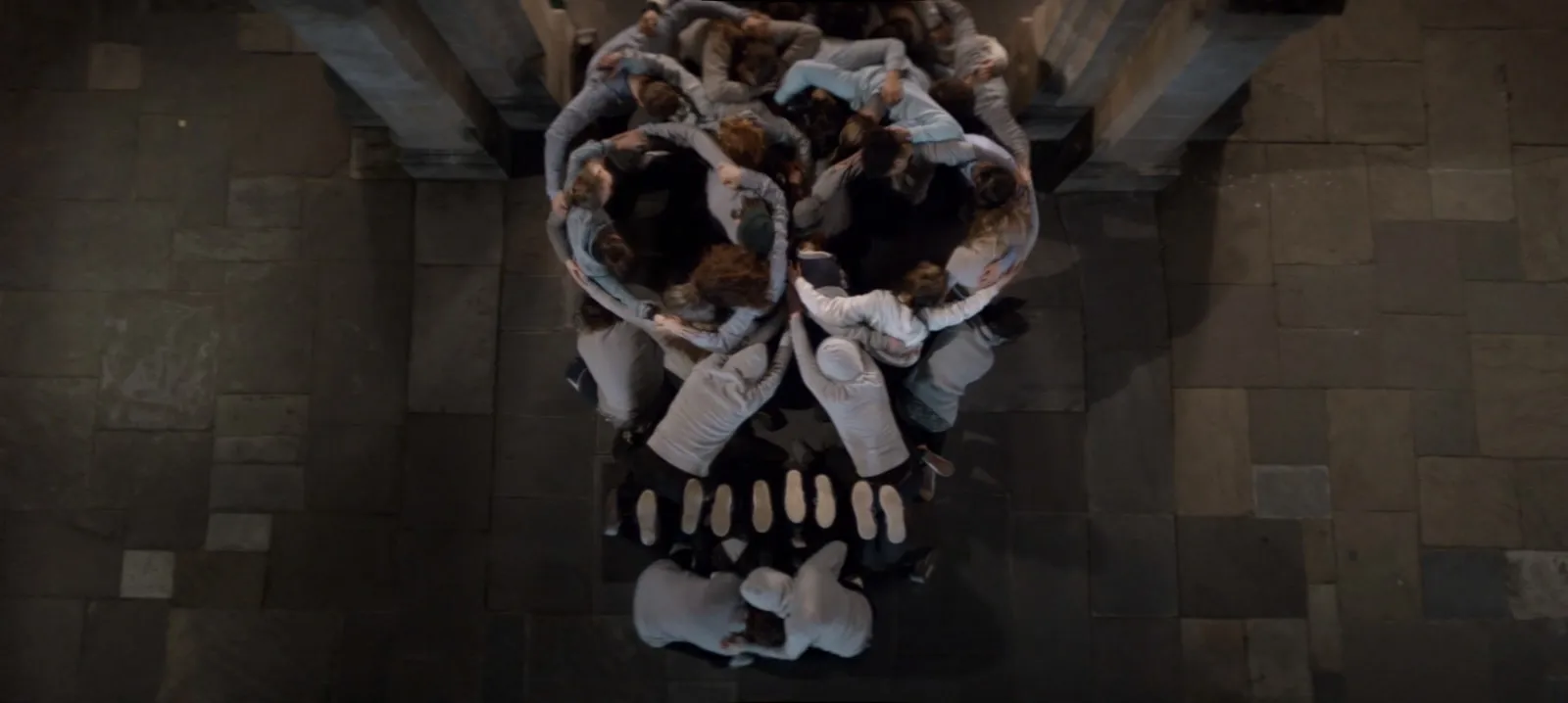 A mass of performers intertwined and suspended together in a dimly lit room.