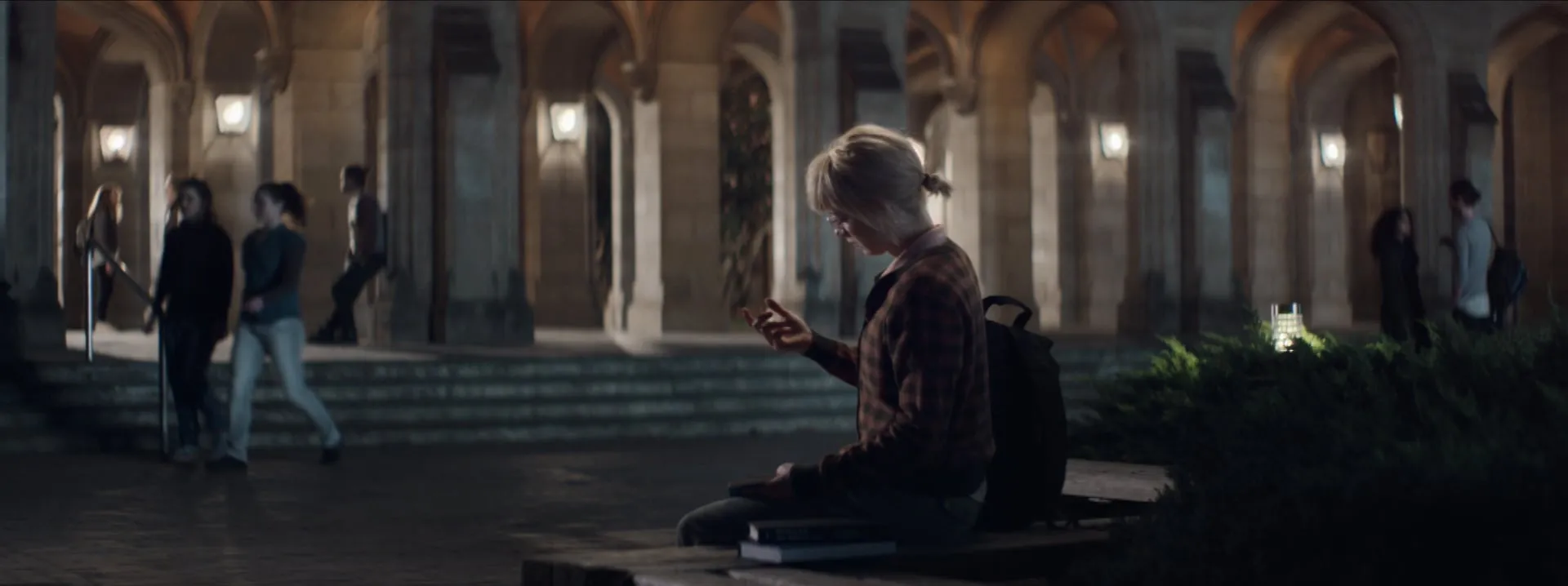 A woman looking at her phone in a dimly lit university courtyard at night