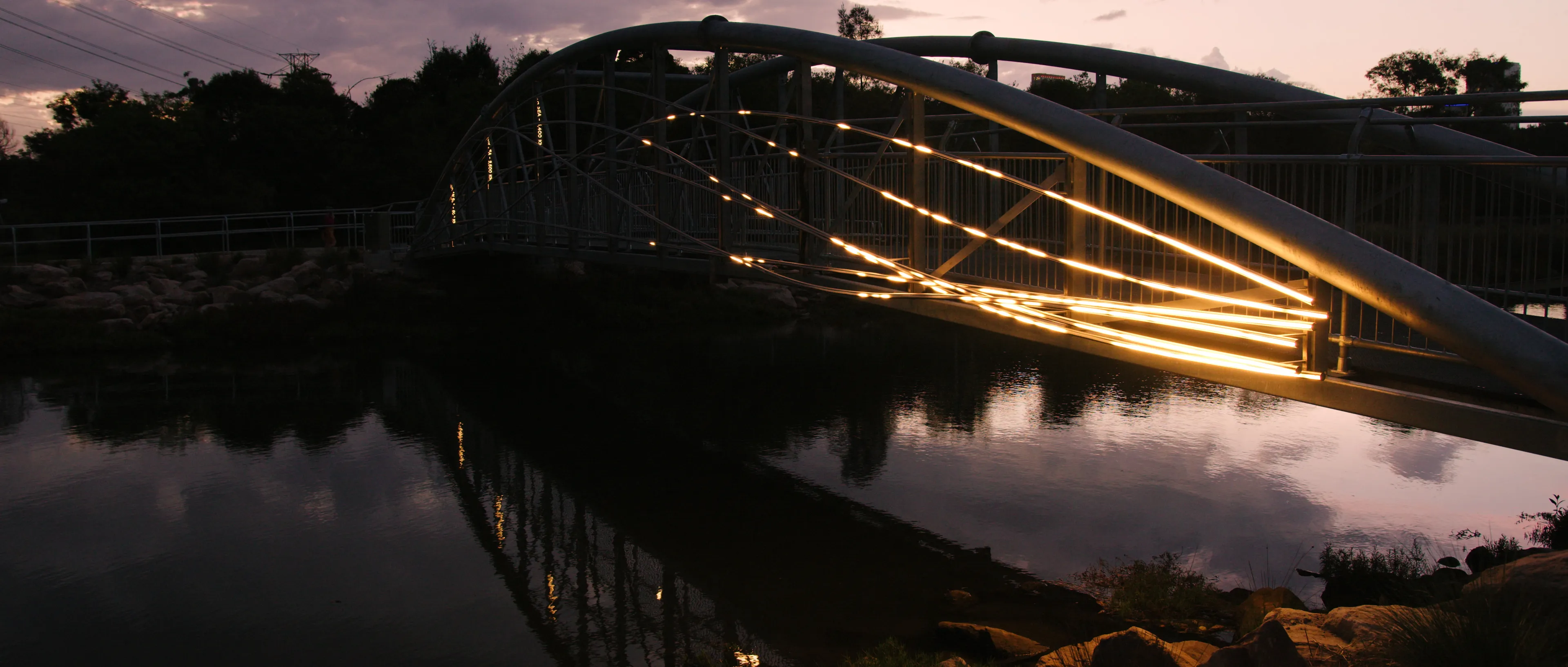 Flyway light installation tracing sweeping illuminated lines across a pedestrian bridge at dusk.