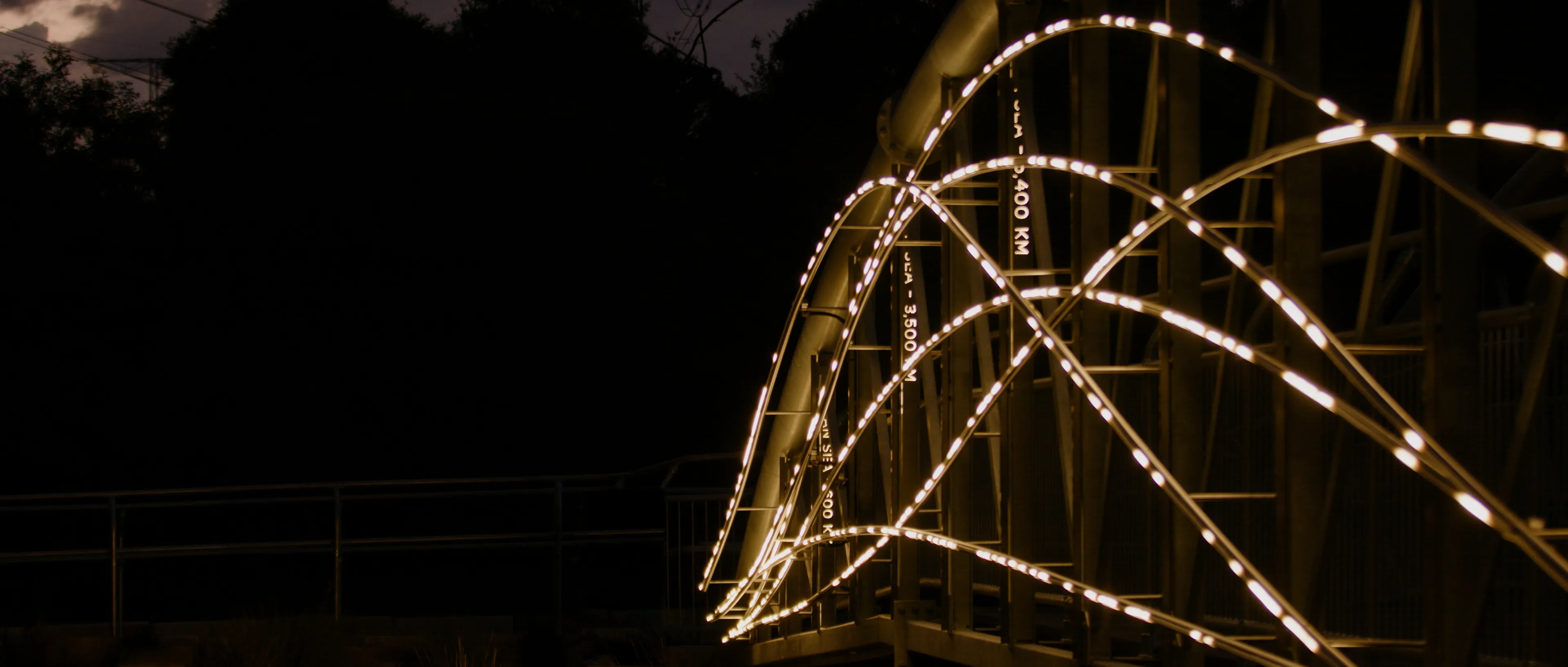 Flyway light installation forming overlapping arcs of light along the structure of the bridge.