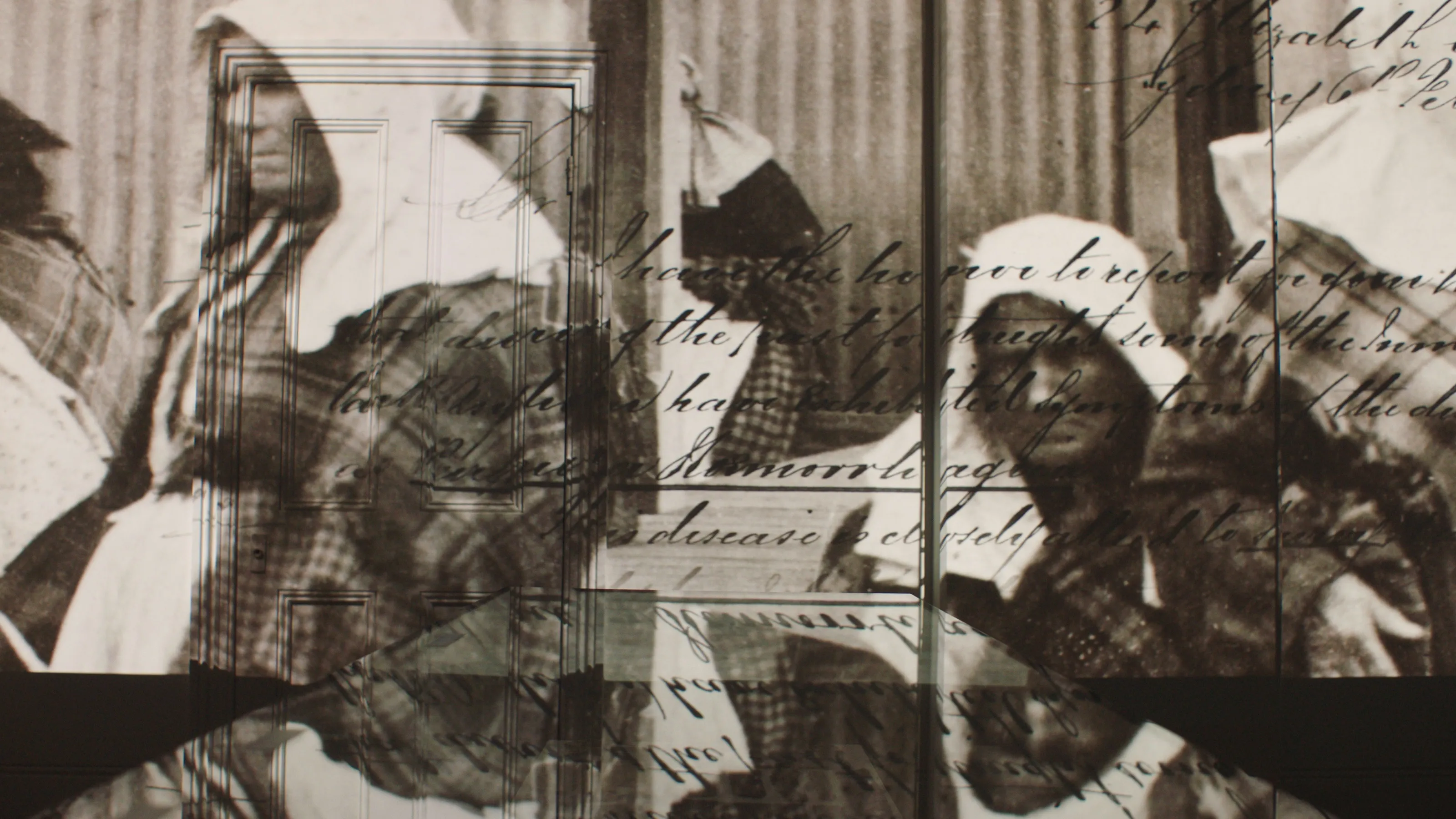 Projected onto an interior wall is some hand-written text and an old black & white photo depicting 4 elderly women.