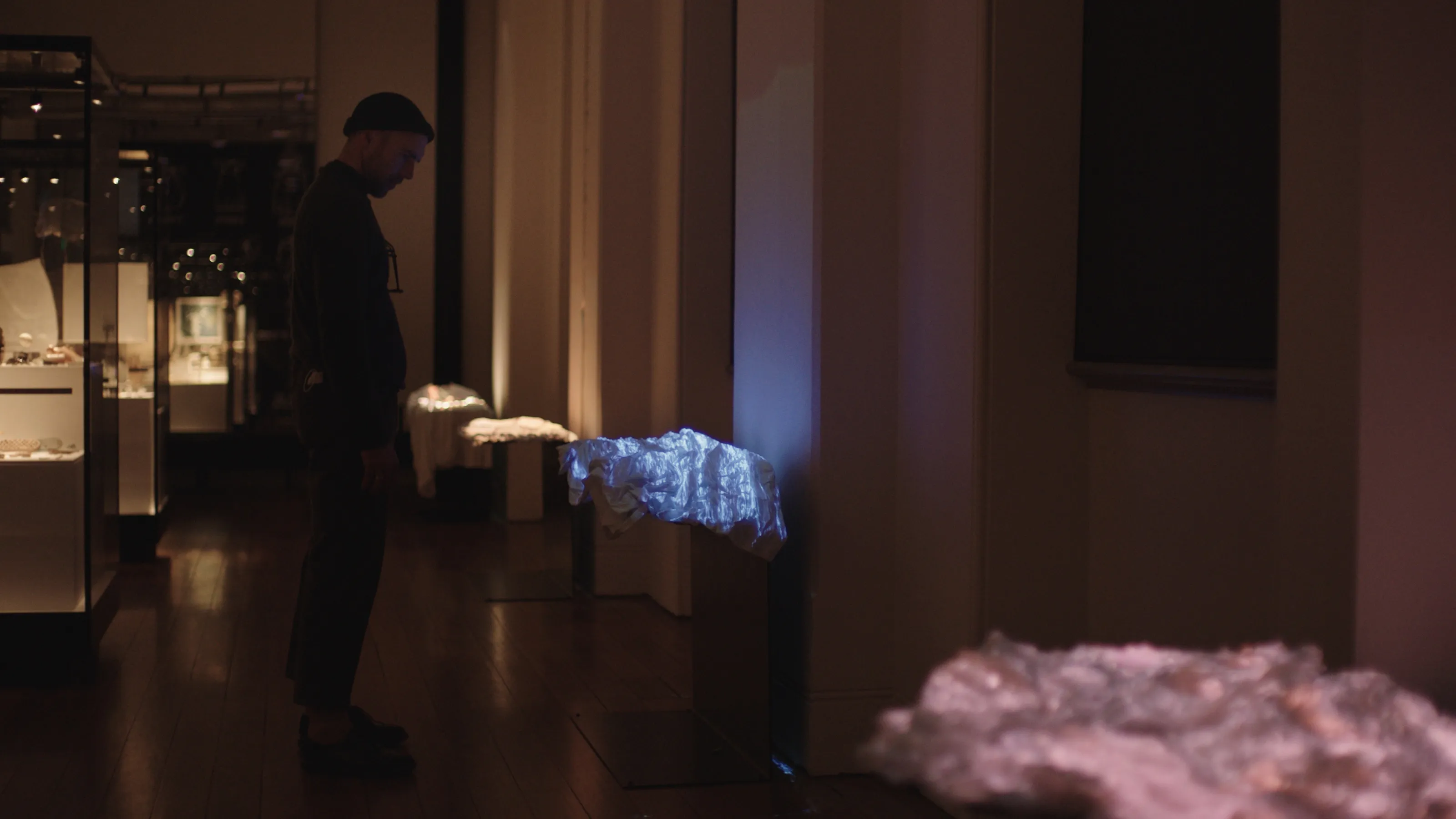 A man stands in front of a museum display consisting of a white dress with blue video imagery projected onto it.