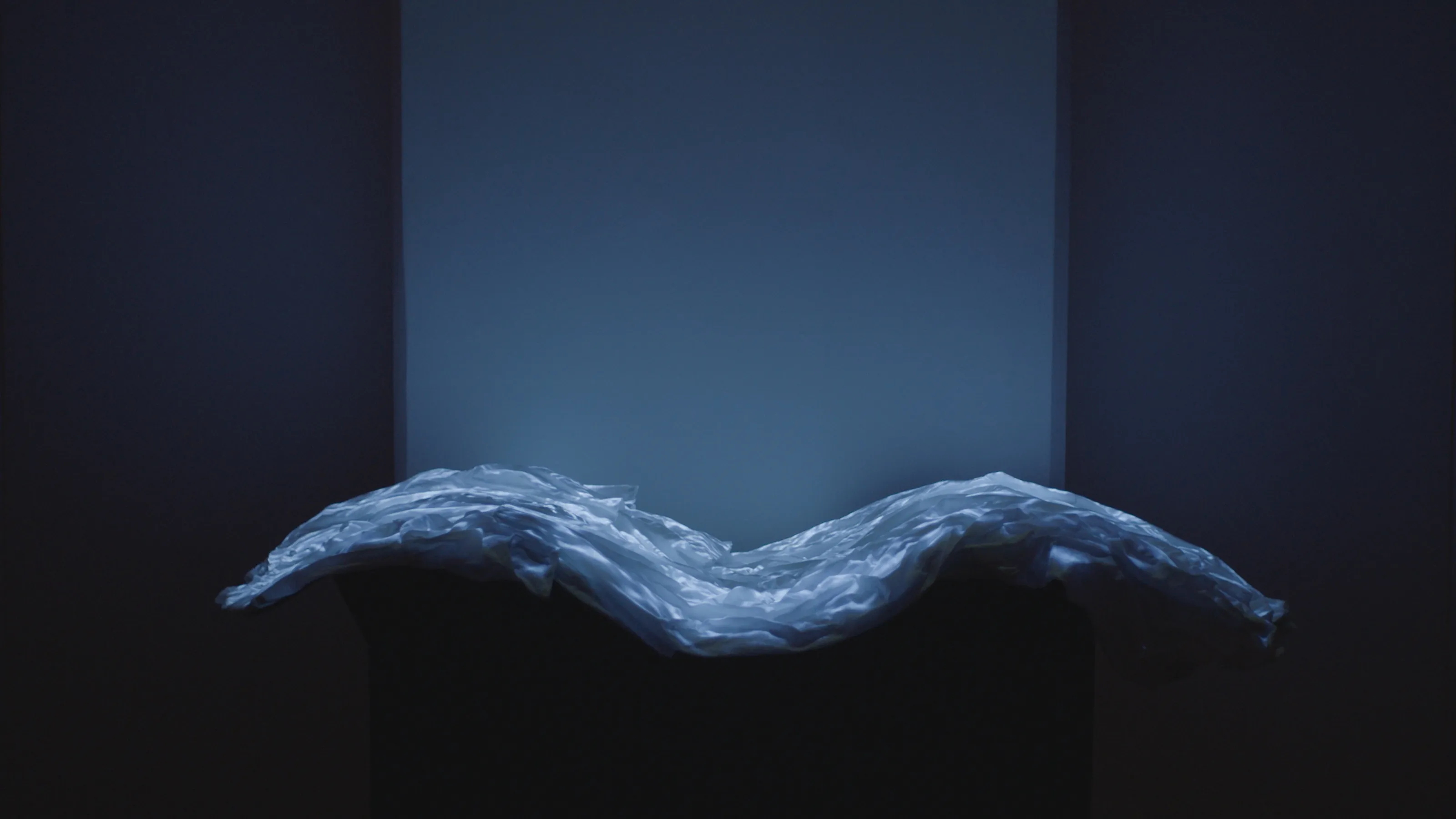 A white dress, in a wave-like curved shape, has blue imagery of water projected on its surface.