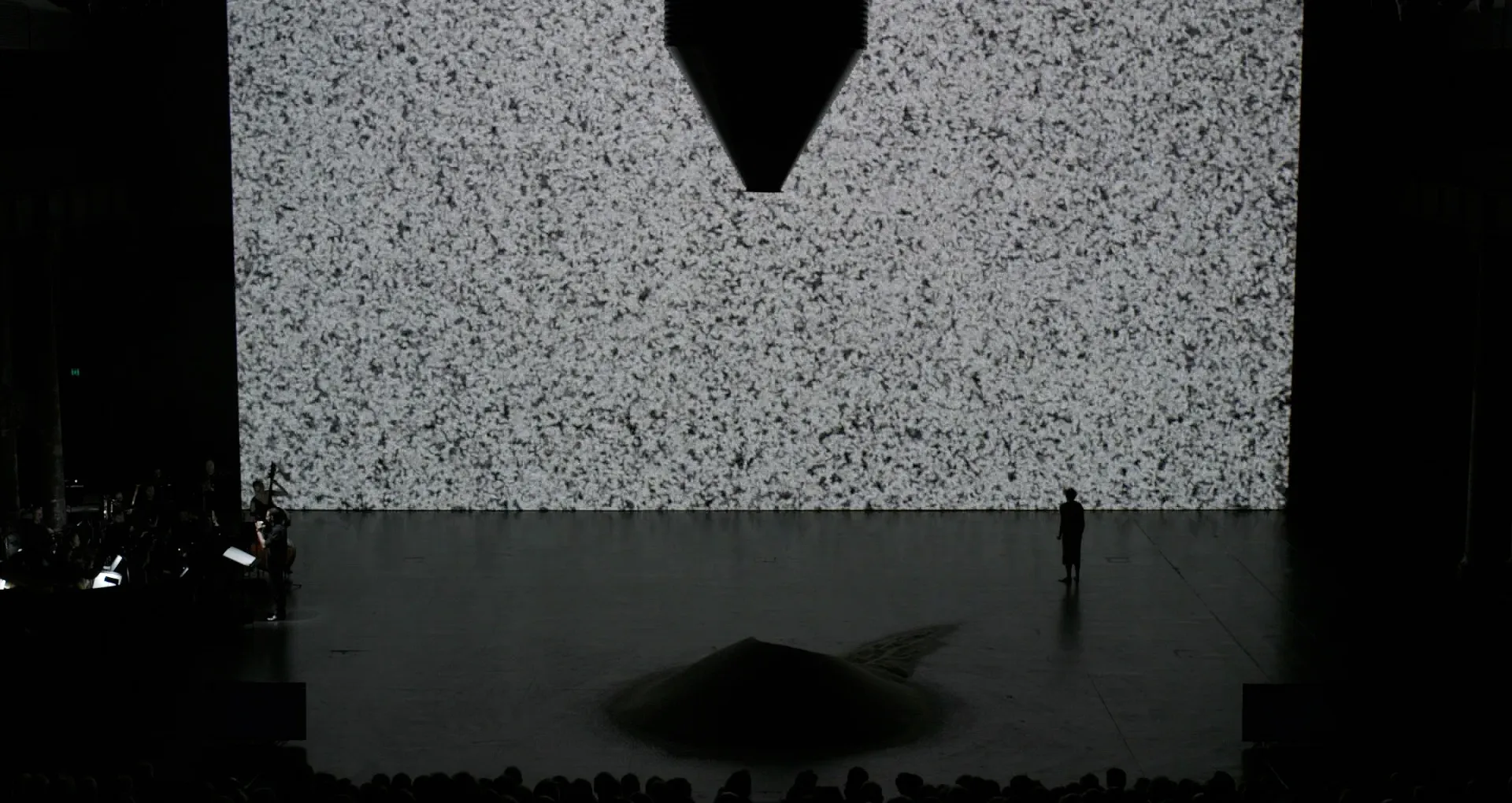A stage with a massive screen, on which there is an image of thousands of particles of rice that looks like white noise.