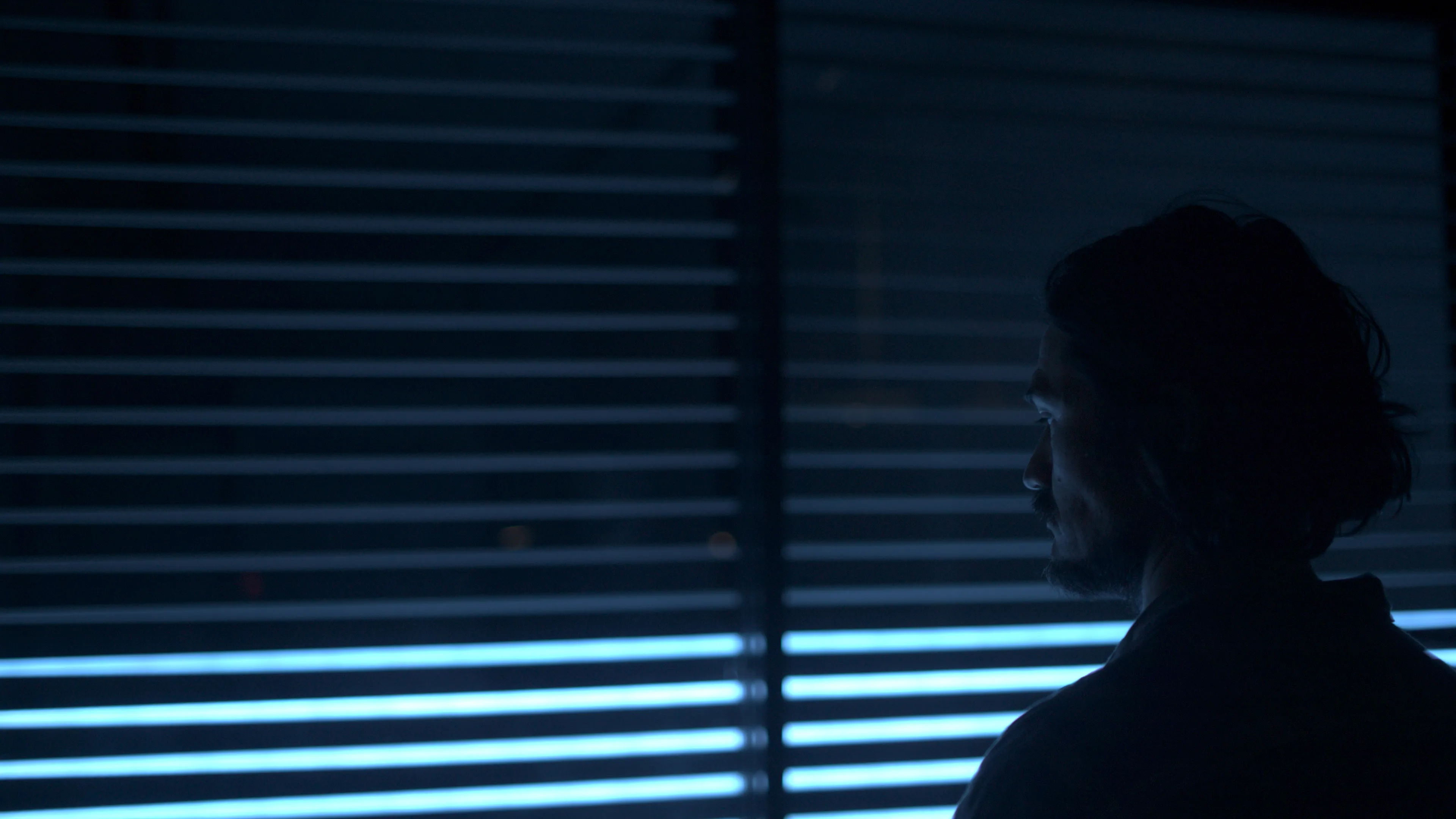 A man stands in front of the light installation artwork at night, illuminated by blue light.