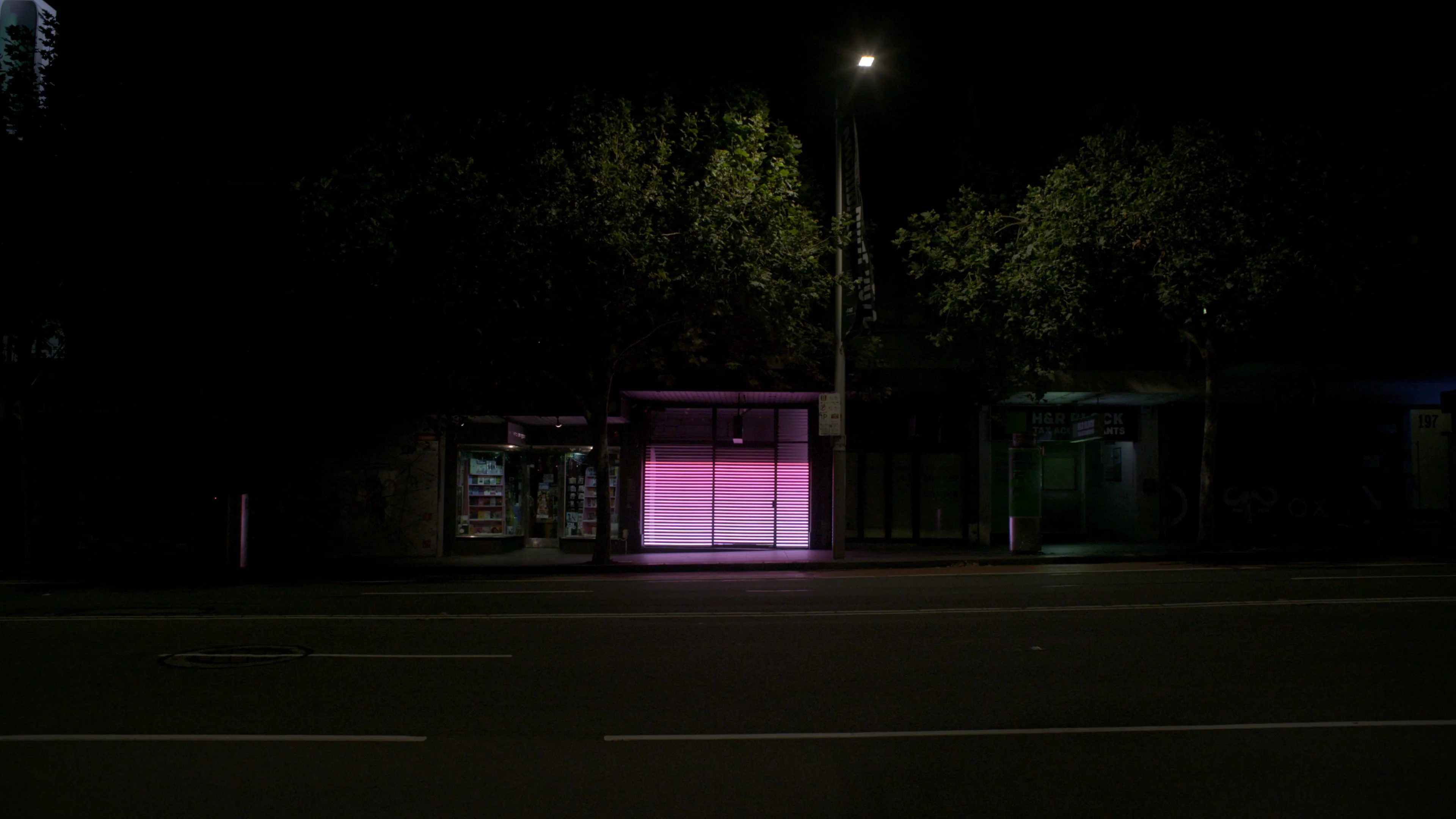 Horizontal pink and white illuminated light strips in a shop-front window in an empty street a night.