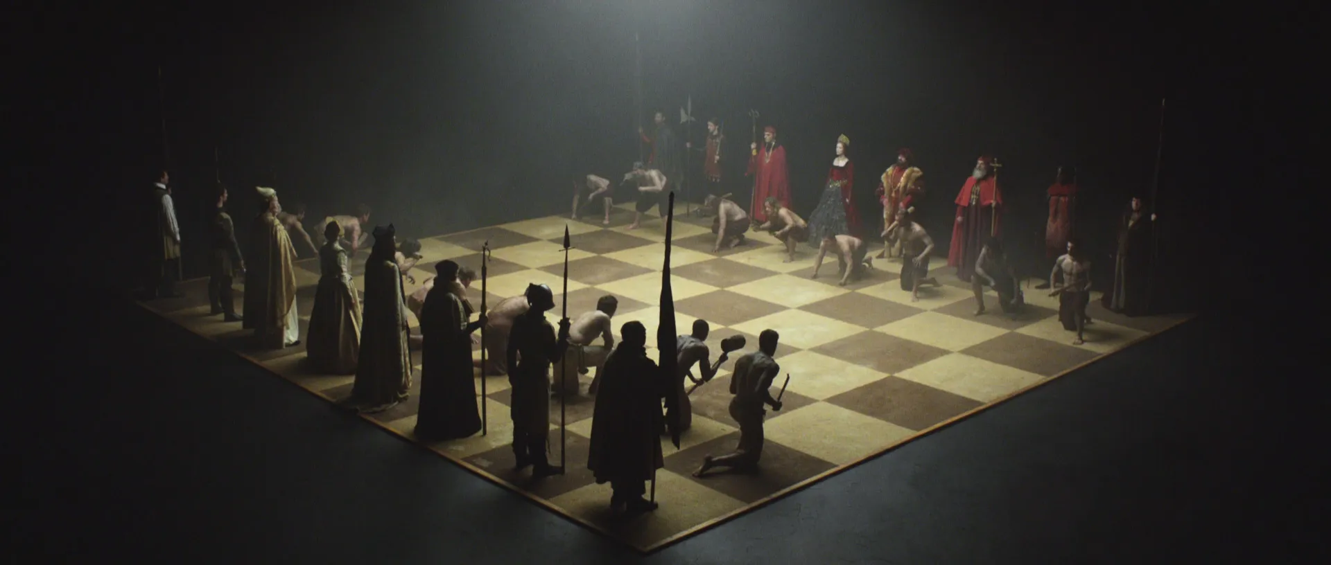 A life-sized chess board in a void with human chess pieces standing in their opening positions.