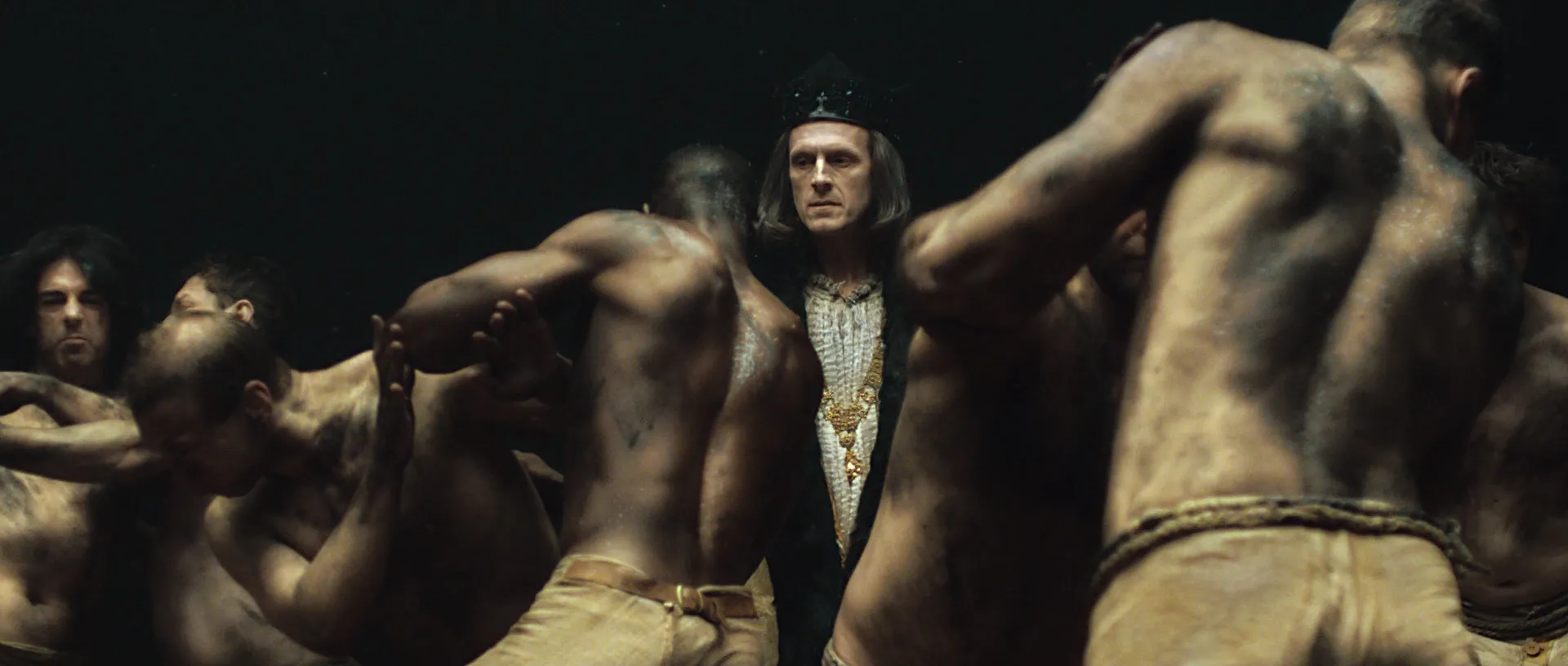 A man dressed as a king is surrounded by six men fighting and wrestling.