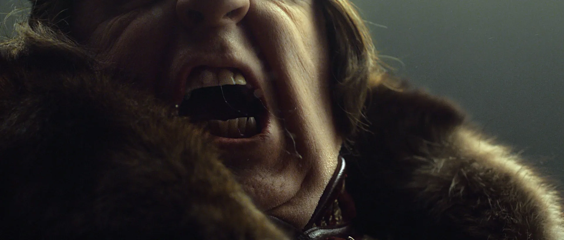 Close-up of a large man wearing fur screaming with spit flying out of his mouth.