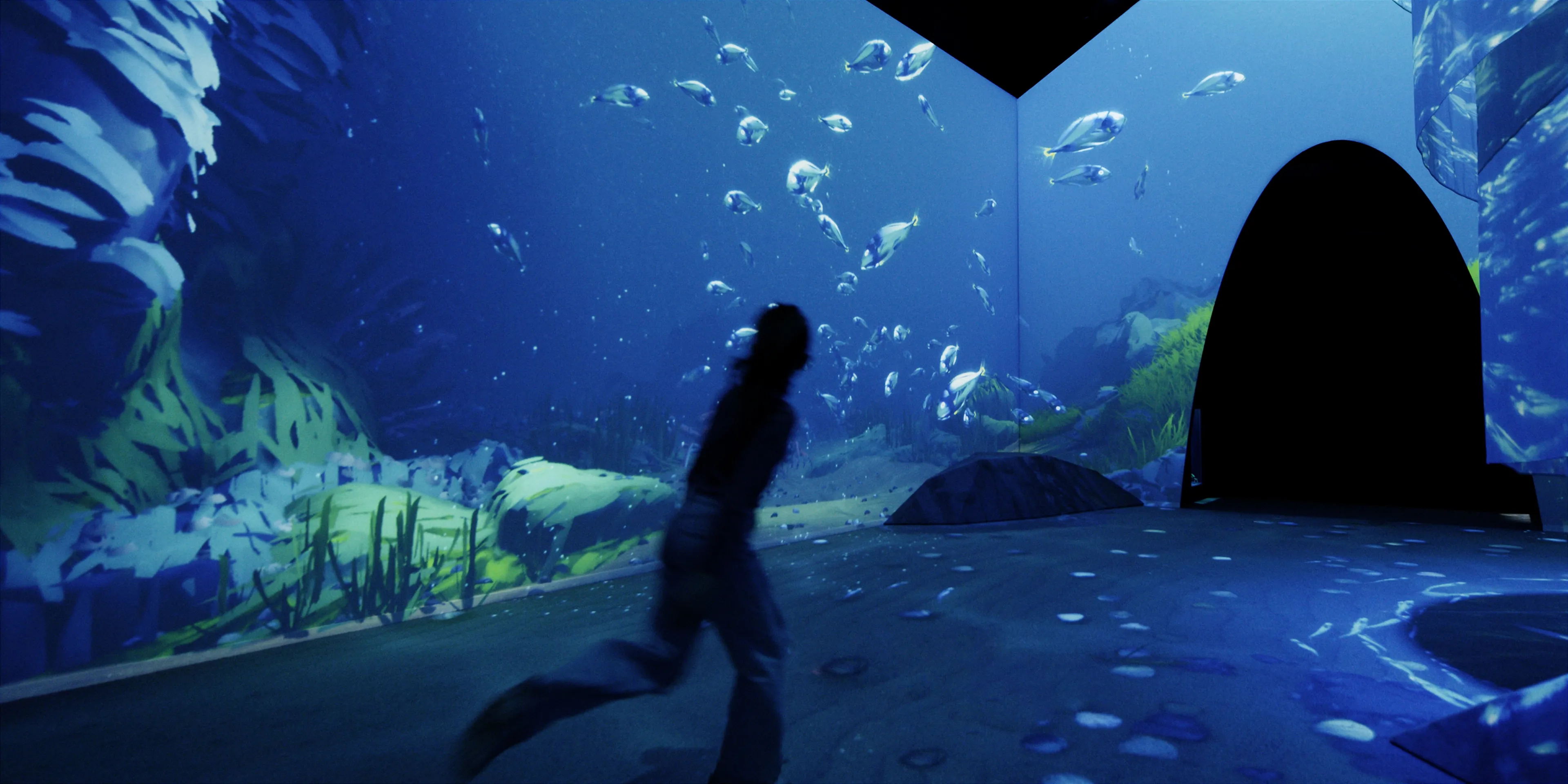 A child runs through an immersive project space depicting a blue underwater world of fish.