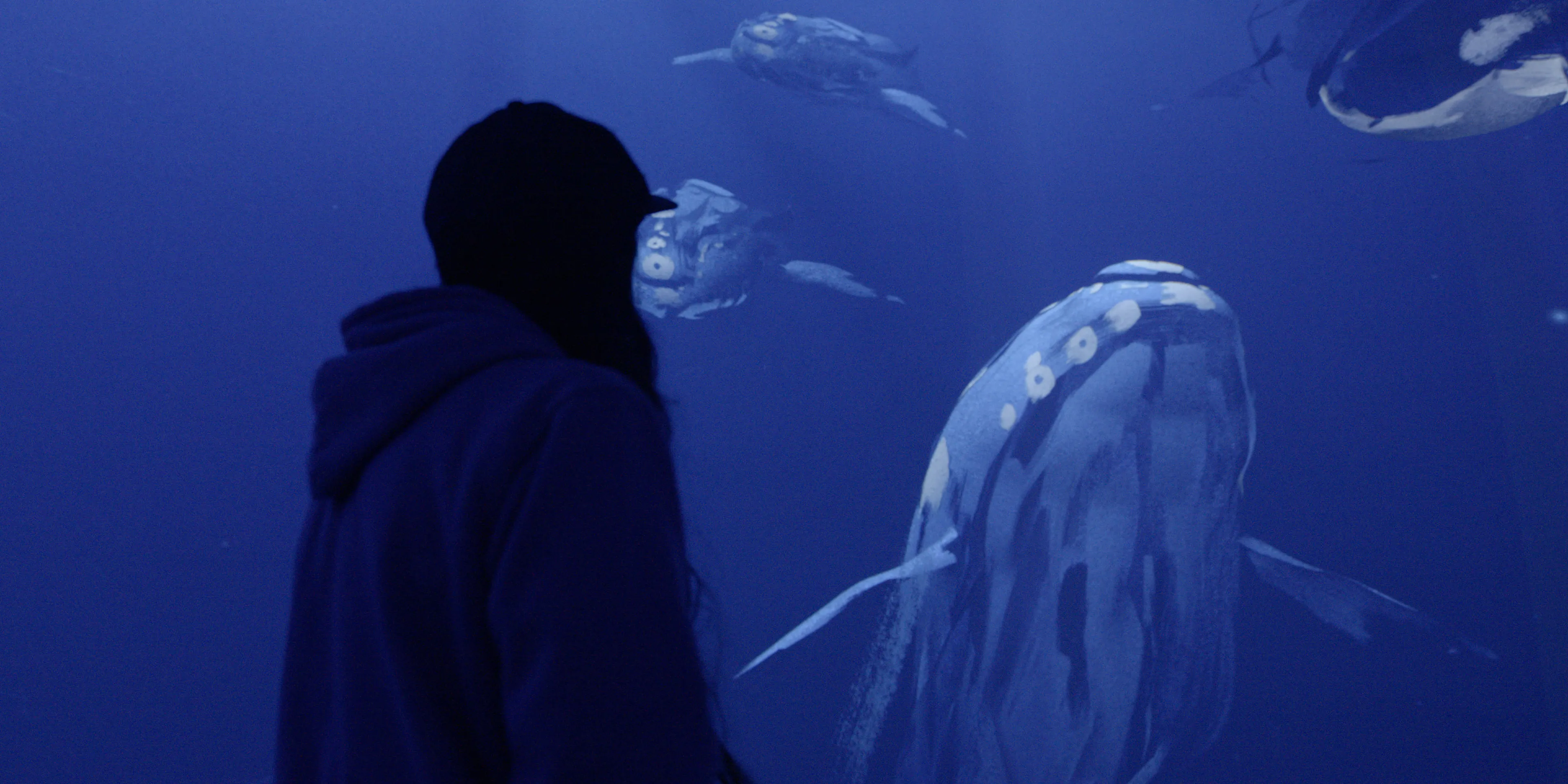 A person stands in front of a painterly-looking image of 4 whales in a blue void of light.